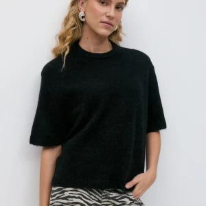 Svart stickad tröja med kort ärm - En svart stickad tröja med korta ärmar och rund halsringning. Tröjan har en avslappnad passform och ribbade kanter vid hals och nederkant. Perfekt att styla med mönstrade byxor för en trendig look.