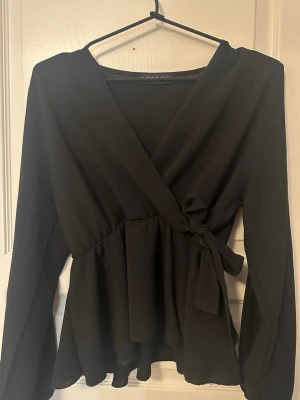 Blus - Omlott  - Snygg svart omlottblus från Missay med långa ärmar och knyt i sidan. Toppen har en v-ringad design och ett lätt utsvängt fall nedtill som ger en snygg siluett. Perfekt att styla med jeans!