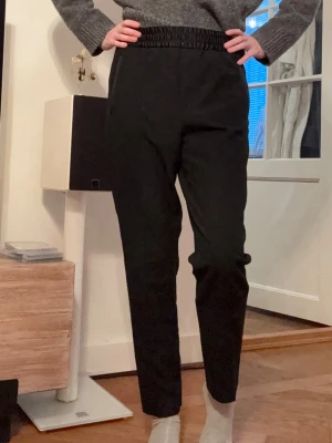 Svarta Kostymbyxor Filippa K Byxor med Resår - Säljer ett par svarta kostymbyxor med hög midja och bred resår i midjan. Kan knytas på insidan. Materialet känns mjukt och skönt mot huden. Något tjockare i materialet vilket gör dem perfekta för vinter, vår och höst. Sparsamt använda. Har fickor på sidorna. Jag är 170 cm för referens.