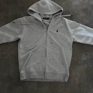 Grå hoodie från Polo Ralph Lauren - Snygg grå hoodie från Polo Ralph Lauren med dragkedja. 