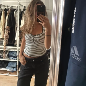 Randig svartvit linnetopp  - Säljer en snygg ärmlös linnetopp med smala svarta och vita ränder. Toppen har en twistad detalj framtill vid bysten och smala axelband. Den är figurnära och croppad, perfekt till jeans eller kjol. Materialet känns mjukt och stretchigt.