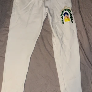 Casablanca byxor  - Vita mjukisbyxor från Casablanca med broderad färgglad logga och motiv på ena benet. Byxorna har snörning i midjan och är tillverkade i mjukt bomullsmaterial. Perfekta för en chill och stilren look. 