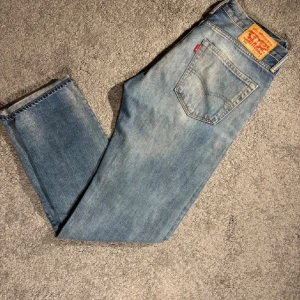 Levi's 501 ljusblå jeans - Klassiska Levi's 501 jeans i ljusblå tvätt med raka ben och ikonisk läderpatch bak. Jeansen har normal passform och är tillverkade i slitstarkt denim. Perfekta för dig som gillar en tidlös och avslappnad stil.