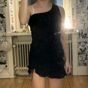 Svart oneshoulder kort klänning - Säljer en svart kort klänning med oneshoulder-design och rynkade detaljer längs sidorna. passar xs-s och 150-165cm