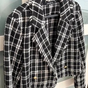 Svartvit rutig kavaj från Gina Tricot - Säljer en svartvit rutig kavaj från Gina Tricot med grov textur och fransade kanter. Kavajen är croppad med dubbelknäppning i guld och har breda slag. Perfekt för dig som vill ha en trendig och edgy look.