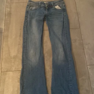 Blå bootcut jeans från Gina Tricot - Snygga blå jeans från Gina Tricot i storlek 152. Modellen har bootcut-ben och klassiska fem fickor med coola detaljer på bakfickorna. Jeansen är i denim med en lätt tvättad look och har normal passform. Perfekta för dig som gillar en avslappnad men trendig stil.