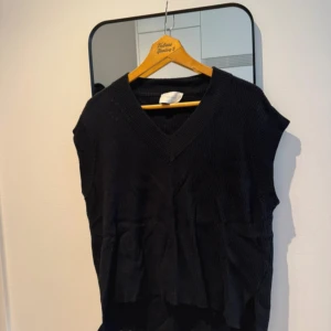 Svart stickad väst från Neo Noir - Svart stickad väst från Neo Noir med  v-ringning och ribbad struktur. Modellen har en klassisk, enkel design utan ärmar. Perfekt att styla över en skjorta eller t-shirt 🖤