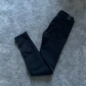 Replay Jeans - Svarta jeans från Replay med klassisk femficksdesign och smal passform. Byxorna har en stilren look med diskreta sömmar och Replay-logga på bakfickan. Perfekta för dig som gillar en enkel och clean stil. Materialet är mjukt och stretchigt jeans.