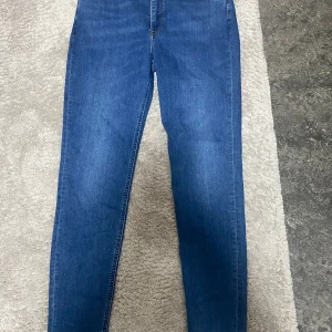 Blå skinny jeans med hög midja - Snygga blå skinny jeans med hög midja och klassisk femficksdesign. Jeansen har en smal passform hela vägen ner och är tillverkade i ett stretchigt denimtyg som sitter tajt men bekvämt. Perfekta till sneakers eller boots. Helt nya, aldrig använda!