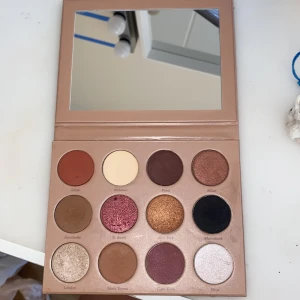 CAIA ögonskuggspalett med spegel - Snygg ögonskuggspalett från CAIA med 12 olika nyanser i både matta och skimrande toner. Färgerna sträcker sig från varma bruna, guldiga och röda till mörka och ljusa nyanser. Paletten har en inbyggd spegel och är perfekt för att skapa olika looks. Några färger är helt oandvända- vilket är anledningen till att jag säljer! Jag har framförallt andvända färgen ”london” så den är lite mer andvänd än de andra. Hela paletten är i nytt skick, pris kan diskuteras :)