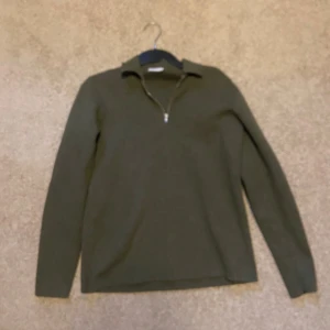 Olivgrön stickad tröja från John Henric - Snygg olivgrön stickad tröja från John Henric med halv dragkedja och krage. Tröjan har lång ärm och är perfekt för lager-på-lager. Enkel och stilren design som funkar till många outfits.
