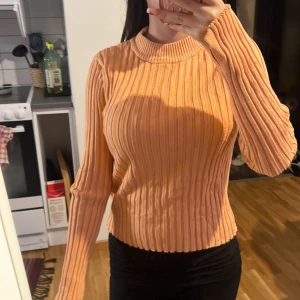 Ribbad orange tröja från Gina Tricot - Superfin ribbad tröja i orange från Gina Tricot. Tröjan har lång ärm med tumhål, högre rund halsringning och är i ett stretchigt material. Perfekt för dig som gillar en slim och bekväm passform.