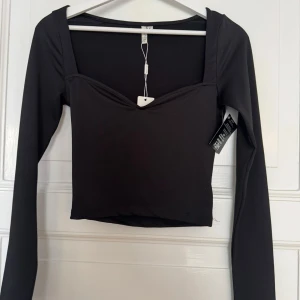 Svart sweetheart-topp från NLY Trend - Säljer en svart långärmad topp från NLY Trend med snygg sweetheart-urringning och croppad passform. Toppen är i stretchigt material och har en stilren, minimalistisk look som passar perfekt till jeans eller kjol.