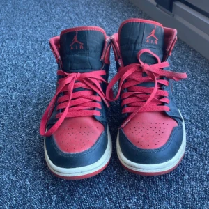 Nike Air Jordan 1 Mid Svart/Röd US7 - Säljer ett par slitna air jordans. Har haft de i ett år och fått många skador men de funkar inte, de är i en röd och svart färd.