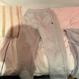 Grå mjukisbyxor från Polo Ralph Lauren - Snygga grå mjukisbyxor från Polo Ralph Lauren med klassisk svart logga broderad på vänster sida. Byxorna har elastisk midja med dragsko och sidofickor, perfekta för chill dagar. Mjukt bomullsmaterial för extra komfort. Passar mig som är 182