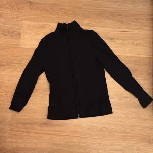 Mörkblå merinoull overshirt från These Glory Days - Mörkblå overshirt från These Glory Days i Superior Merino-ull. Tröjan har hel dragkedja framtill, hög krage och långärmad design. Stilren och enkel look som funkar till många outfits. Materialet är mjukt och värmande merinoull. S men sitter som XS. Ny pris 1000.