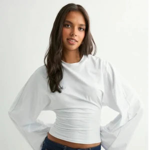 Vit långärmad topp med ballongärmar - Säljer en helt oanvänd vit långärmad topp från Lager 157 med ballongärmar och rund hals. Modellen är croppad och har en loose passform över ärmarna. Materialet är mjuk bomull som känns skönt mot huden.