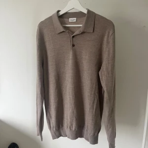  pikétröja från John Henric - Snygg beige pikétröja från John Henric. Tröjan har klassisk krage, två knappar framtill och långa ärmar med ribbade muddar. Perfekt för dig som gillar stilrena och tidlösa plagg med en clean look. Modellen är 180cm