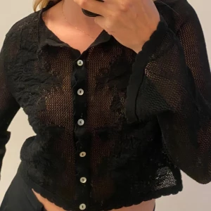 Svart virkad tröja från Zara - Svart virkad tröja från Zara med lång ärm, croppad passform och snygga knappar framtill. Skjortan har spetsdetaljer och vågig kant vid ärmslut och nederkant.🖤💘