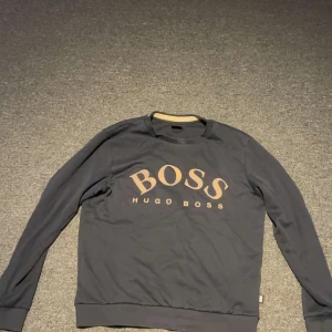 Mörkblå långärmad tröja Hugo Boss - Mörkblå långärmad tröja från Hugo Boss med stor beige logga på bröstet, säljer den pågrund av att den är för liten för mig, hör av er ifall ni har några mer frågor