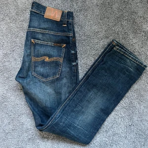 Blå jeans från Nudie Jeans - Snygga blå jeans från Nudie Jeans med klassisk femficksdesign och kontrastsömmar på bakfickorna. Jeansen har en rak passform och är tillverkade i slitstarkt denimtyg av bomull. Perfekta för dig som gillar en tidlös och avslappnad stil. Storlek 31 W 32 L fitts 30 W 32 L
