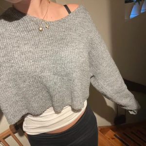 Grå croppad stickad tröja - Säljer en grå, croppad stickad tröja med loose passform och offshoulder-design. Tröjan har lång ärm och är perfekt för dig som gillar en chill och avslappnad stil. Mjuk och skön att bära, passar till både jeans och kjol.