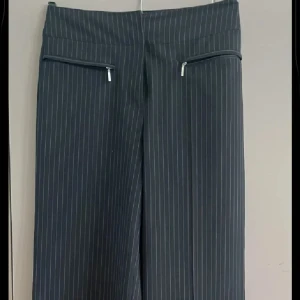 Randiga svarta kostymbyxor wide fit - Snygga svarta kostymbyxor med smala vita ränder och bred midja. Byxorna har två dragkedjefickor framtill och ett wide fit-ben som ger en cool och avslappnad look. Perfekta att styla med sneakers eller boots.