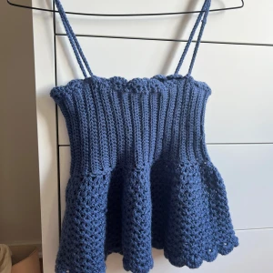 Blå virkad linnetopp med volang - Söt blå virkad linnetopp med smala axelband och volang nertill. Toppen har ribbad överdel och en luftig, mönstrad nederdel med vågig kant. 