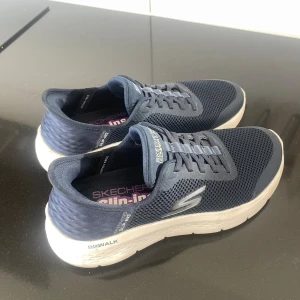 Skechers Go Walk Slip-ins sneakers marinblå - Marinblå Skechers Go Walk Slip-ins sneakers med vit sula och mesh-ovandel. Skorna har elastisk snörning och är tillverkade i syntetmaterial för en luftig och bekväm känsla. Perfekta för dig som vill ha en sportig och stilren look. Använda högst 10 gånger. Hör av dig vid frågor! (Går att pruta vid snabb affär)