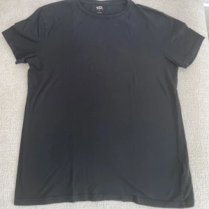 Svart basic t-shirt från 157 - Enkel svart t-shirt från 157 med rund halsringning och korta ärmar. Tillverkad i mjuk bomull för en skön känsla. Perfekt till jeans eller shorts för en clean och stilren look.