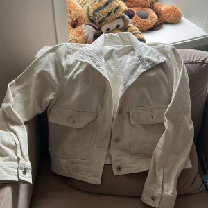 Vit jeansjacka med stora fickor - Snygg vit/krämvit jeansjacka med klassisk krage och stora fickor framtill. Silver knappar och den passar super till höst eller till våren! Använd bara en gång men annars är den i super bra skick!