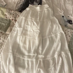 Vit långkjol från H&M - Superfin vit långkjol från H&M med bred smock i midjan. Kjolen är tillverkad i en mjuk blandning av viskos och polyamid med foder i polyester. Perfekt för en luftig och avslappnad stil.