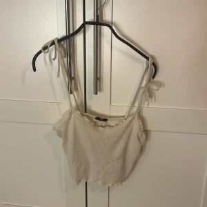 Beige ribbad linnetopp från Even&Odd - Säljer en ljusbeige croppad linnetopp från Even&Odd med ribbad struktur och smala axelband som knyts på axlarna. Toppen har en söt volangkant både upptill och nedtill, perfekt för sommarens alla tillfällen. Supersnygg att styla med jeans eller kjol!