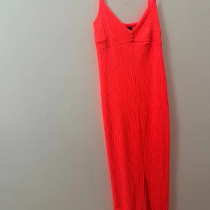 Neonrosa/röd långklänning med slits framifrån  - Neonrosa långklänning med smala axelband och v-ringning framtill. Helt ny aldrig använt den, prislappen är kvar, super fin verkligen men den är för stor på mig, storlek S men strechig, den är även genomskinlig och är i från Gina tricot men verkligen super snygg och den va känd under en period men för stor på mig som sagt.  