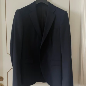 Mörkblå kostym från Tiger of Sweden - Snygg mörkblå kostym från Tiger of Sweden, klassisk modell med kavaj och matchande kostymbyxor. Kavajen har smal passform, två fickor fram och stilrena knappar. Materialet är ull och polyester, vilket ger en lyxig känsla och bra komfort. Nypris ca 6 000