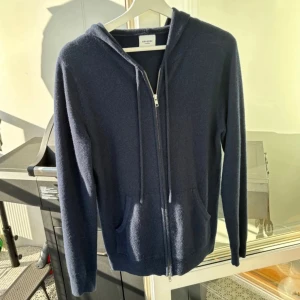 Mörkblå hoodie i kashmir från John Henric - Snygg mörkblå hoodie från John Henric i 100% kashmir. Tröjan har dragkedja framtill, huva med snörning och två fickor. Perfekt för dig som vill ha något både stilrent och riktigt mjukt. Klassisk passform och långärmad modell.