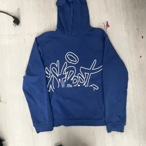 Blå hoodie med grafiskt tryck H&M - Blå hoodie från H&M med vit grafisk text framtill. Klassisk känguruficka och huva. Skön och avslappnad passform, perfekt för chill dagar. Tillverkad i mjuk bomullsmix.