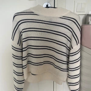 Randig stickad tröja från H&M XS - Superfin stickad tröja från H&M i storlek XS. Den är vit med svarta horisontella ränder, har en ribbad krage och muddar samt lång ärm. Perfekt för lager-på-lager och chill stil.