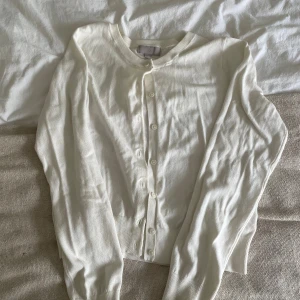Vit kofta från H&M i bomull, M - Klassisk vit kofta från H&M i storlek M. Den har rund halsringning, långa ärmar och knäppning framtill med matchande vita knappar. Tillverkad i mjuk bomull, perfekt att slänga över en topp eller klänning.
