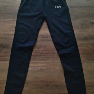 Tränings byxor ICIW - Svarta tights från ICANIWILL med logga framtill. De har en tight passform och är gjorda i ett stretchigt syntetmaterial som passar perfekt för träning. Hög midja och ribbad linning för extra komfort.