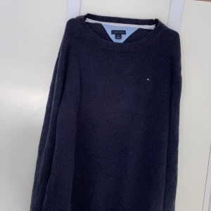 Mörkblå stickad tröja Tommy Hilfiger XL - Mörkblå stickad tröja från Tommy Hilfiger i storlek XL. Klassisk rund halsringning och diskret logga broderad på bröstet. Perfekt för lager-på-lager och passar till jeans eller chinos.