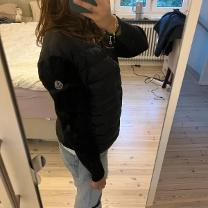 Svart Moncler cardigan  - Säljer en svart Moncler cardigan med quiltad front och ärmar i mjuk ullmix. Jackan har dragkedja framtill och klassisk Moncler-logga på ena ärmen. Perfekt för kyliga dagar och riktigt snygg till jeans eller dressade byxor. Jackan är en S men skulle säga att den passar XS mer. Den har blivit tvättad en gång därför har texten på lapparna suddats ut lite (se sista bilden). Armarna sitter lite tajt💘🫐