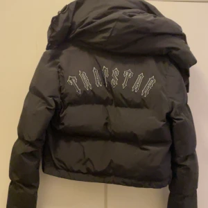Trapstar pufferjacka  - Svart pufferjacka från Trapstar i storlek XS. Jackan har en croppad passform, stor huva och dragkedja framtill. På ryggen finns Trapstar-logga i vitt och på bröstet en rund patch. Perfekt för kalla vintrar! (Pris går att diskutera lämna ett prisförslag) 