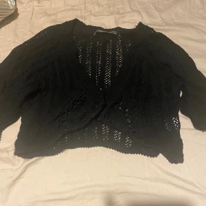 Svart stickad kofta från Culture XL - Svart stickad kofta från Culture i storlek XL. Koftan har ett öppet, virkat mönster med snygga detaljer och knäppning framtill. Perfekt att slänga över en topp för en chill och trendig look. Långärmad och luftig modell.