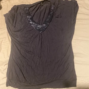 Mörkgrå topp med paljetter från Amisu - Snygg mörkgrå topp från Amisu med djup v-ringning dekorerad med glittriga paljetter. Toppens material är mjukt och lätt, perfekt för dig som gillar lite extra bling. Modellen är ärmlös och har en avslappnad passform som sitter skönt.