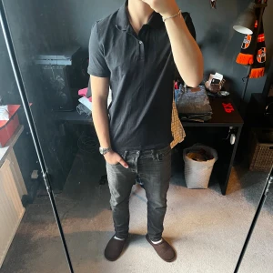 Pikétröja  - Säljer en svart pikétröja med klassisk krage och knappar framtill. Tröjan har korta ärmar och en slim passform som sitter snyggt på kroppen. Perfekt för dig som vill ha en enkel men stilren look. Skriv för mer bilder