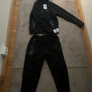 Nike tech - Svarta mjukisbyxor från Nike i storlek M. Byxorna har dragsko i midjan, diskret Nike-logga på benet och dragkedjeförsedda fickor med snygga detaljer. Perfekta för chill eller träning, tillverkade i mjukt bomullsmaterial.