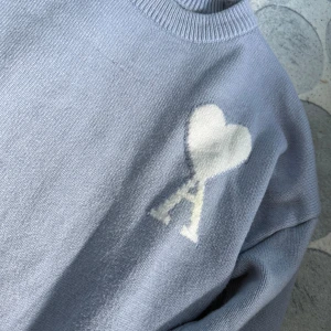 Ljusblå stickad tröja från Ami - Snygg ljusblå stickad tröja från Ami med ett vitt hjärta och bokstaven A broderat på bröstet. Tröjan har ribbade muddar vid ärmslut och hals, samt långärmad passform. Perfekt för dig som gillar stilrena detaljer och mjuka material.