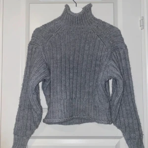 Grå ribbad polotröja från H&M - Säljer en grå stickad polotröja från H&M i storlek XS. Tröjan har en hög krage, ribbad struktur och långa ärmar. Materialet känns mjukt och värmande.