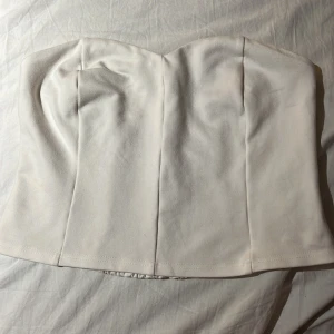 Vit tub topp  - Säljer en stilren vit bandeau tubtopp med hjärtformad byst och smockad rygg för extra stretch. Toppen är ärmlös och har en slät framsida med markerade sömmar. Perfekt att matcha med jeans eller kjol för en clean look.